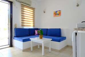 Ein Zimmer mit einem blauen Sofa, einem weißen Tisch, einer Topfpflanze, einem Bild an der Wand und einem Fenster mit Jalousien.