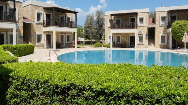 A poolside view of a hotel with stone facades, balconies, and a clear blue pool.