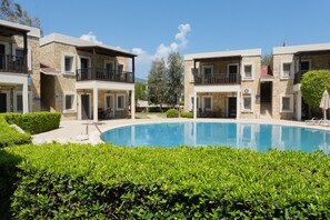 A poolside view of a hotel with stone facades, balconies, and a clear blue pool. - Aktur Cove Apart Hotel (Bodrum)