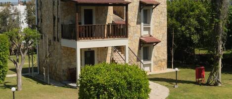 A two-story building with a stone facade, a balcony, and a small garden area.