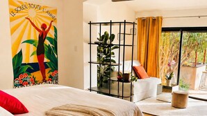 A bedroom with a bed, a sofa, a plant shelf, and a view through a large window. - Villa with all comforts, ideal for families or friends: swimming pool, ps5, paddles (Solliès-Pont)