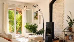 A living room with a sofa, a coffee table, a fireplace, a bookshelf, and a view of greenery outside. - Villa with all comforts, ideal for families or friends: swimming pool, ps5, paddles (Solliès-Pont)