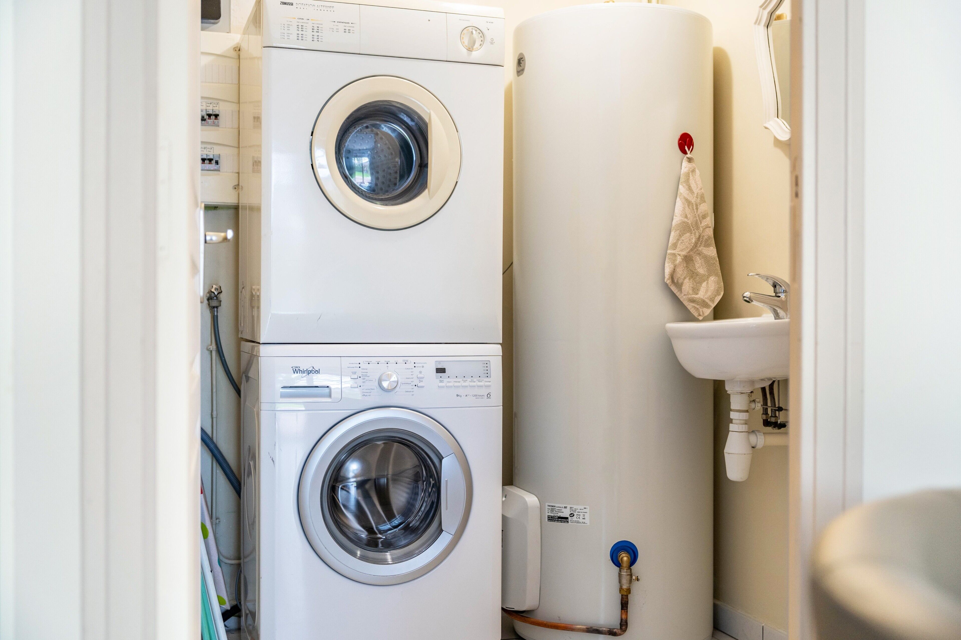 A compact laundry area with two stacked washing machines and a water heater.