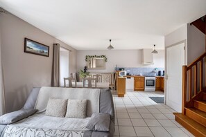 Una sala de estar con sofá, una mesa de comedor, sillas, una cocina con armarios y electrodomésticos, y una escalera.