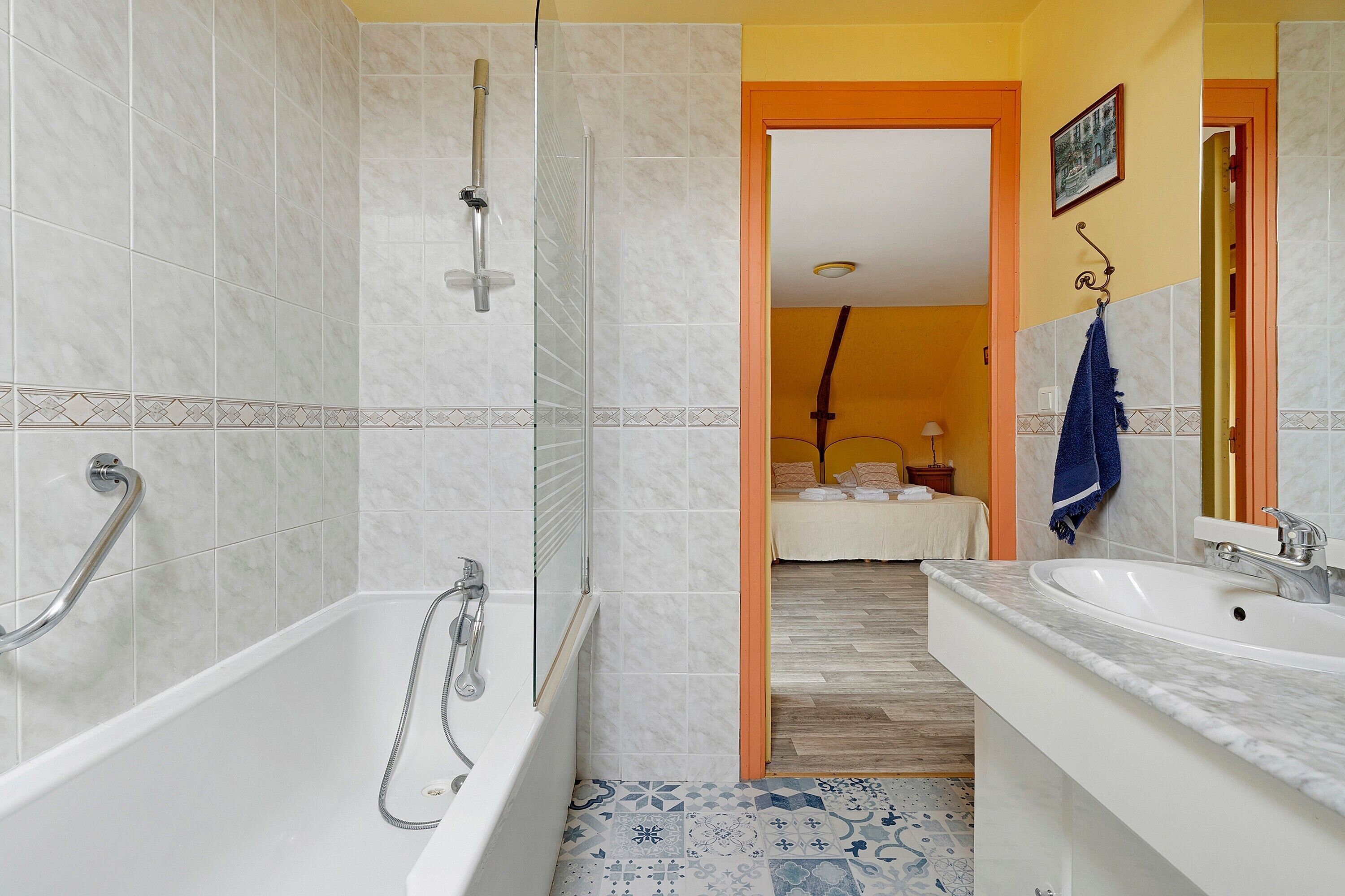 Een badkamer met een bad, douche en wastafel, met een gang die leidt naar een slaapkamer.