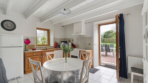 Une cuisine avec une table à manger, des chaises, une horloge et une vue sur le jardin.