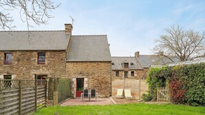 Un bâtiment en pierre avec une courClose, une porte en bois et un petit espace extérieur aménagé pour s’asseoir.