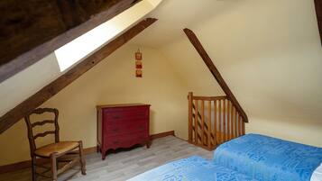 A bedroom with a sloped ceiling, a wooden chair, a red dresser, and a bed with a patterned bedspread.