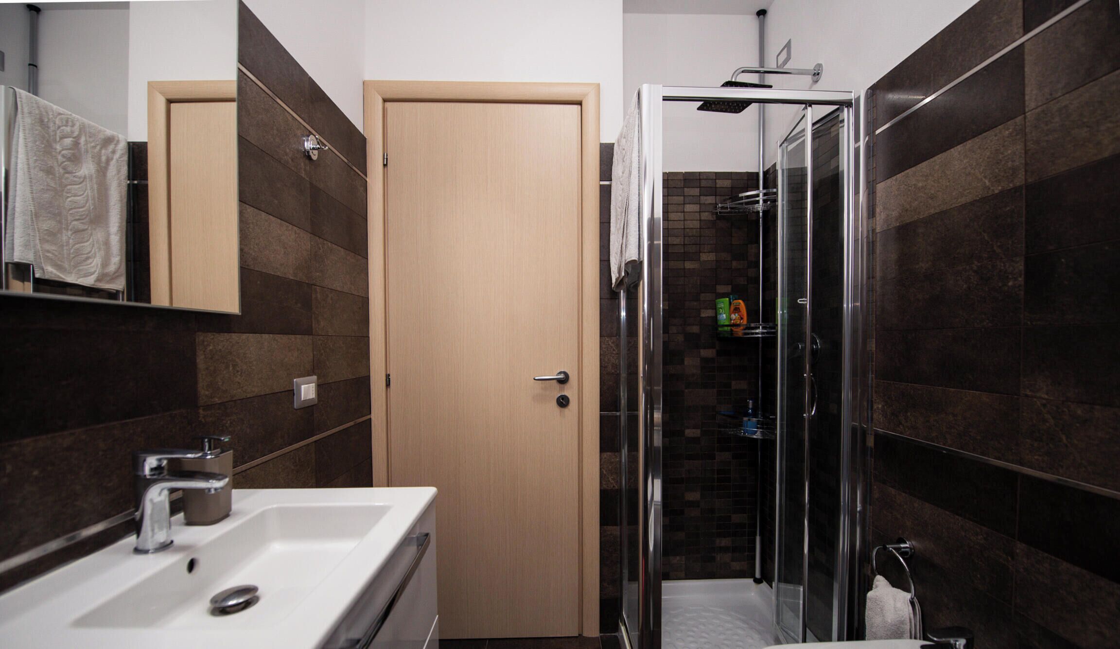 Une salle de bain comprenant un lavabo, un miroir, un porte-serviettes, une douche et une porte.
