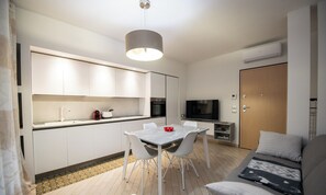 A modern kitchen with white cabinets, a dining table, and chairs. There is a TV, a microwave, and an oven. - Appartamento Sole (Polpenazze del Garda)