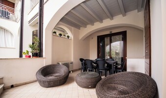A covered outdoor seating area with wicker furniture, a table, and a radiator.