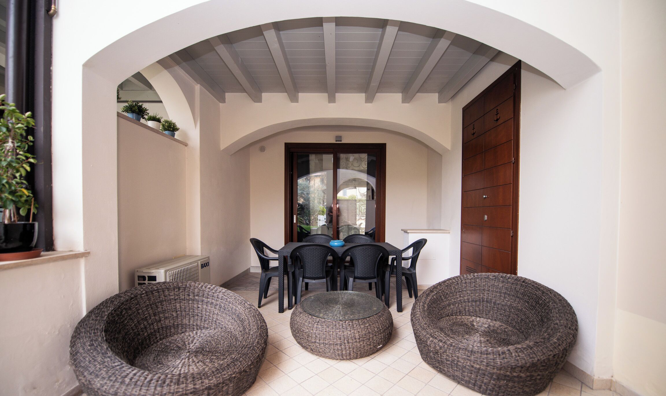 Un patio al aire libre con una mesa, sillas, una puerta de madera y muebles de mimbre.