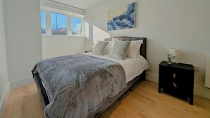 A bedroom with a bed, a nightstand, a window, and a painting on the wall. - Luxury Wimbledon 2B2B | Cinema • Gym • Games Room (London)
