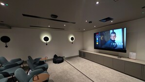 A modern home theater with a large flat-screen TV, comfortable seating, and ambient lighting. - Luxury Wimbledon 2B2B | Cinema • Gym • Games Room (London)