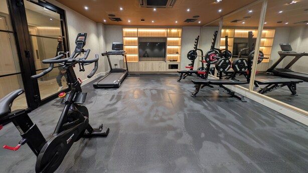 A gym with exercise equipment, a mirrored wall, and a ceiling with recessed lighting. - Luxury Wimbledon 2B2B | Cinema • Gym • Games Room (London)