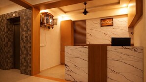 Un'area reception con parete in marmo, scrivania reception in legno, televisore a parete e ventola a soffitto.