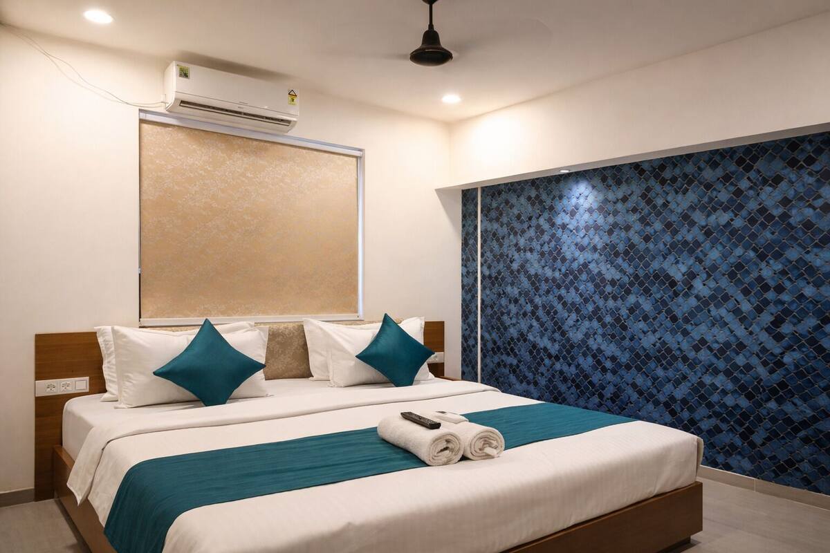 A hotel room with a bed, a window, an air conditioning unit, and a patterned wall.