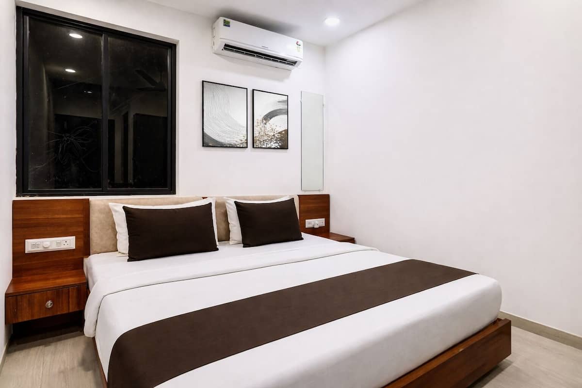 A modern hotel room with a large bed, wooden headboard, bedside tables, and a window with blinds.