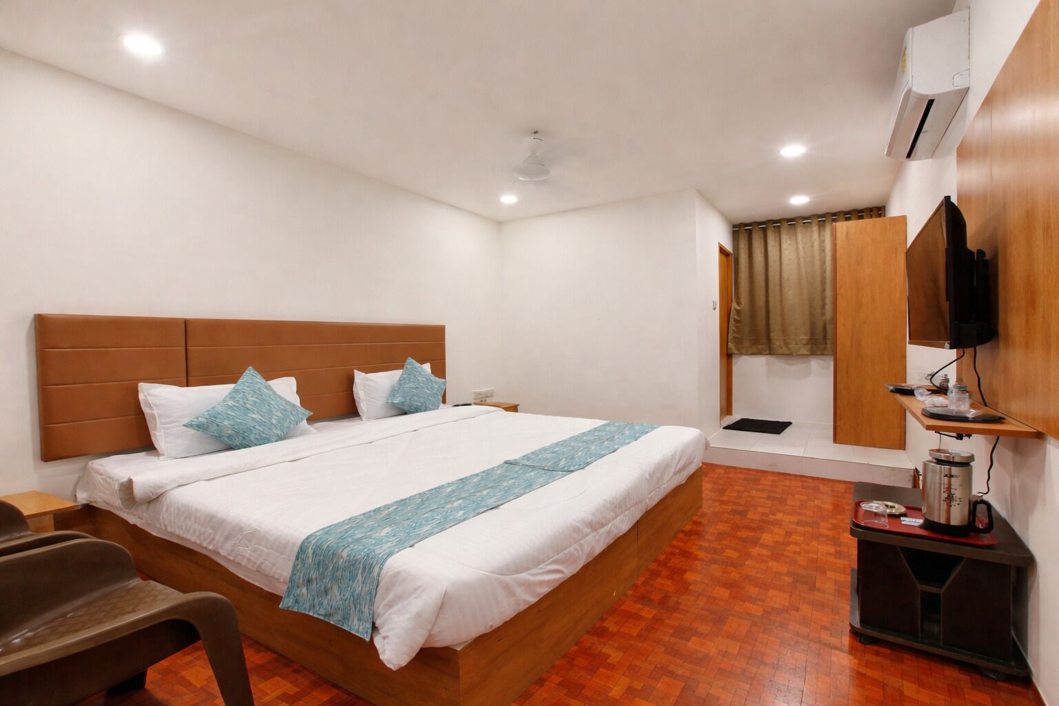A hotel room with a large bed, a desk, a chair, an air conditioning unit, and a television.