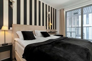 Ein Hotelzimmer mit Bett, Nachttisch, Lampe, Fenster mit Blick und einer Wand mit vertikalen Streifen.