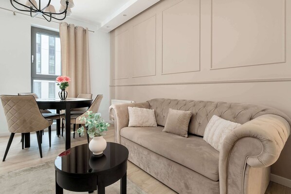 Ein Wohnzimmer mit einem beigen Sofa, einem schwarzen Couchtisch und einem Essbereich mit Tisch und Stühlen.