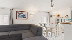 Una sala de estar moderna con un sofá seccional gris, un comedor con sillas blancas y una mesa, y una cocina con microondas y armarios.