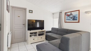 Un salón con un televisor de pantalla plana, un sofá gris, un armario blanco y un cuadro en la pared.