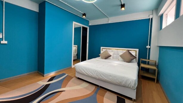 A room with a bed, a blue wall, a patterned rug, and a ceiling light fixture. - Queen On Street Guesthouse (Phuket)
