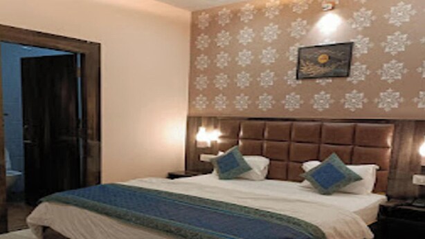 A bedroom with a large bed, two bedside tables, a headboard, and a wall with a floral pattern. - HOTEL NEEL GAGAN  (Varanasi)