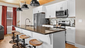 Eine moderne Küche mit weißen Schränken, Edelstahlgeräten, einer Granitarbeitsplatte und einer Holztheke mit Hockern.