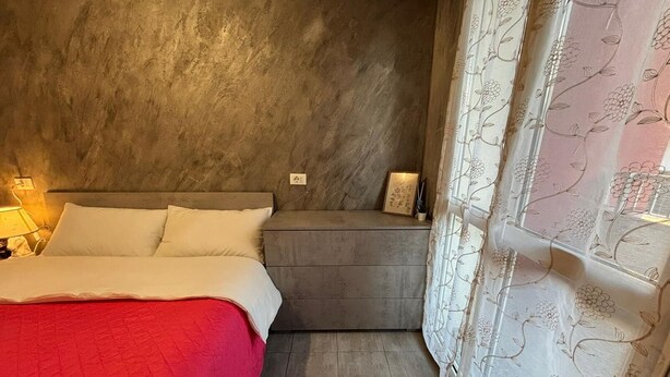 Ein Schlafzimmer mit Bett, Nachttisch, Lampe und einem kleinen Regal mit Bilderrahmen.