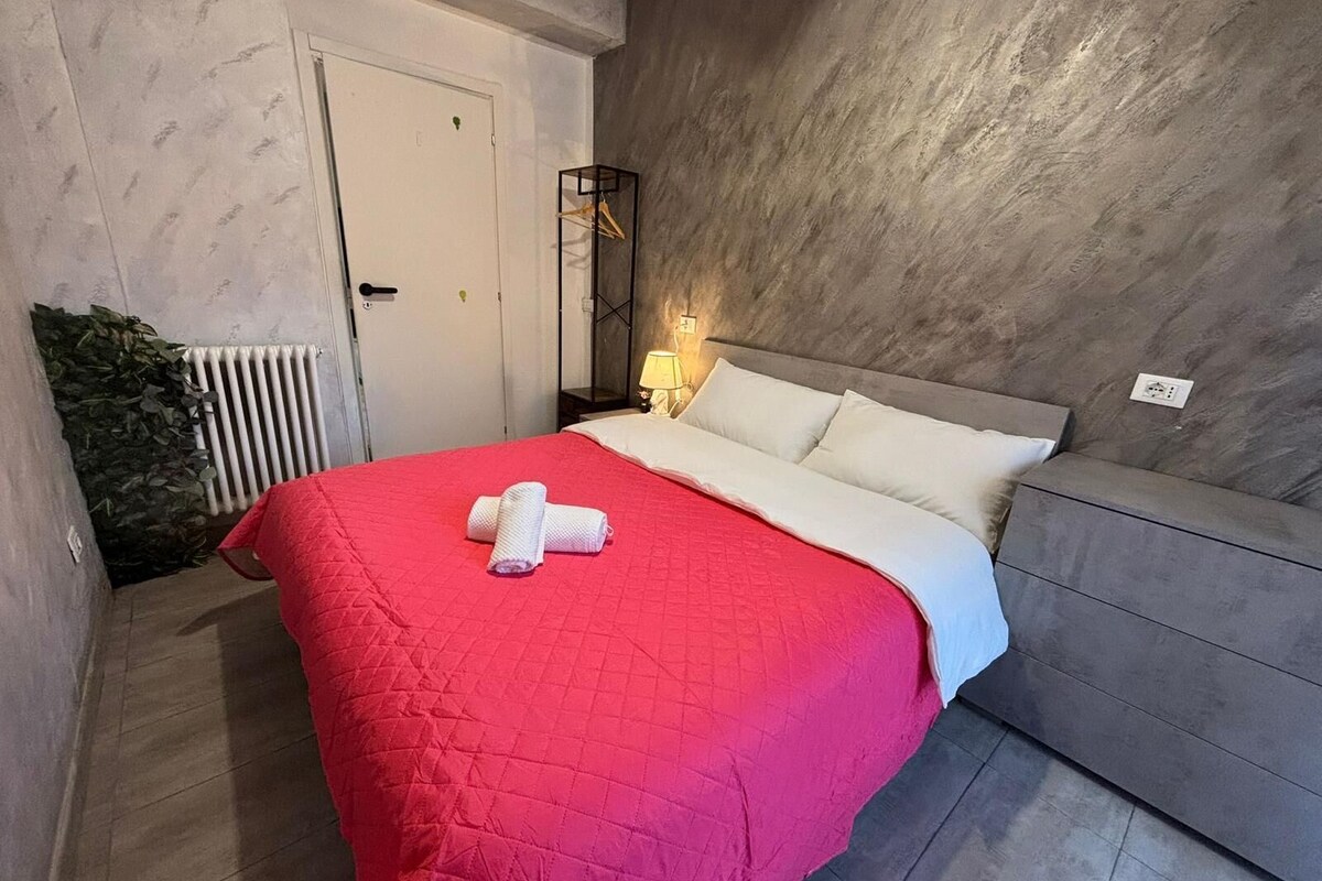 Un dormitorio con una cama, una mesita de noche, una lámpara y un sofá gris.