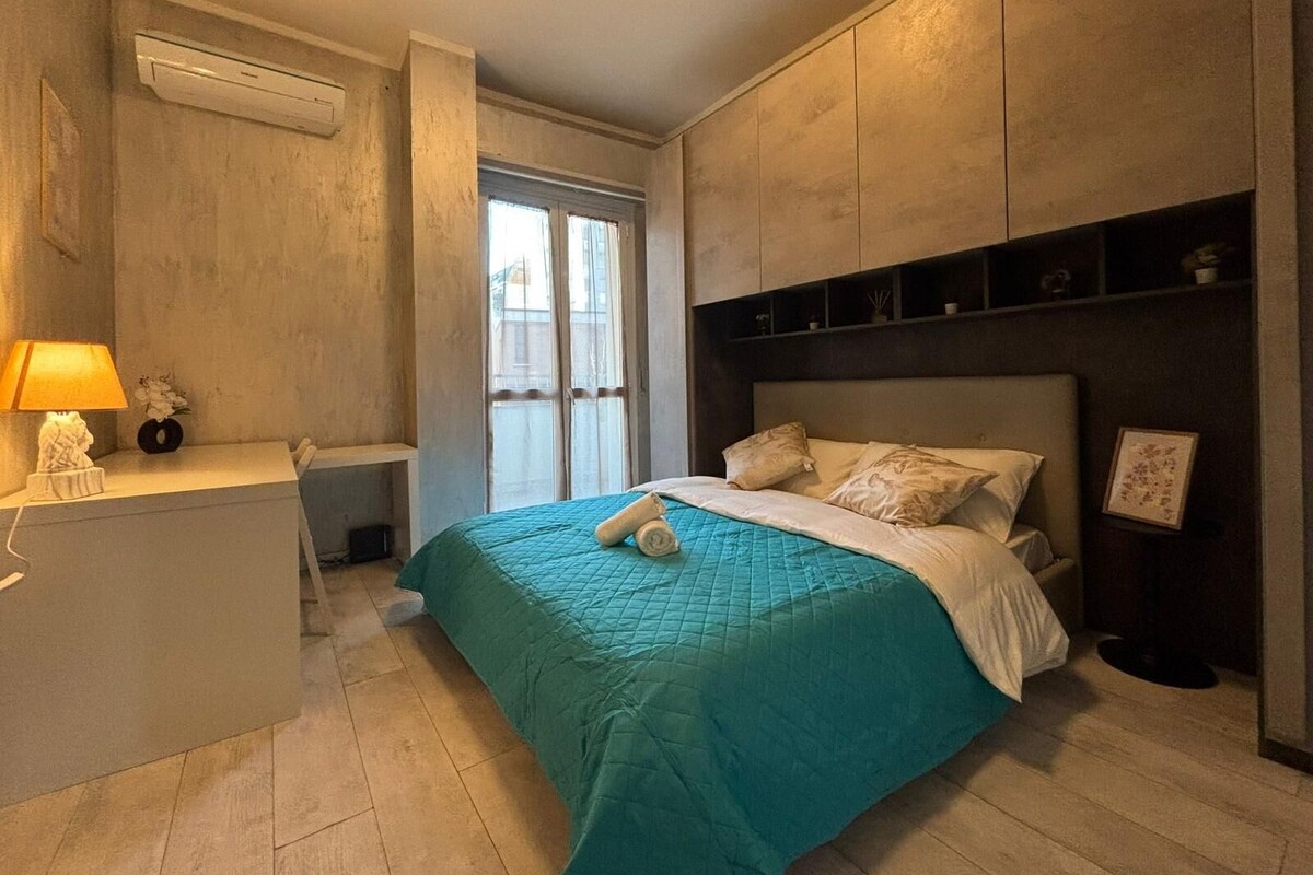 Un dormitorio con cama, mesita de noche, lámpara y ventana.