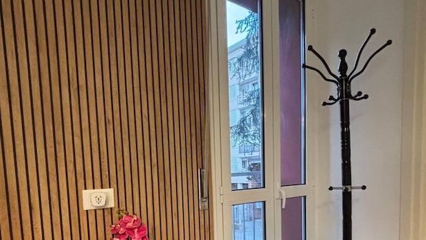Een kamer met een wand van houten latten, een grijze bank, een klein tafeltje met roze bloemen en een kapstok.