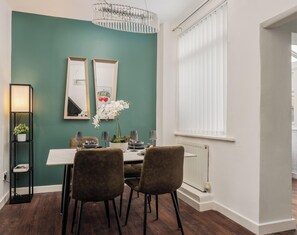 A dining area with a table, chairs, a chandelier, a potted plant, and a window with blinds. - Cosy 2 bed home for Contractors, Getaways and Business Travellers w/Free Parking (St Helens)