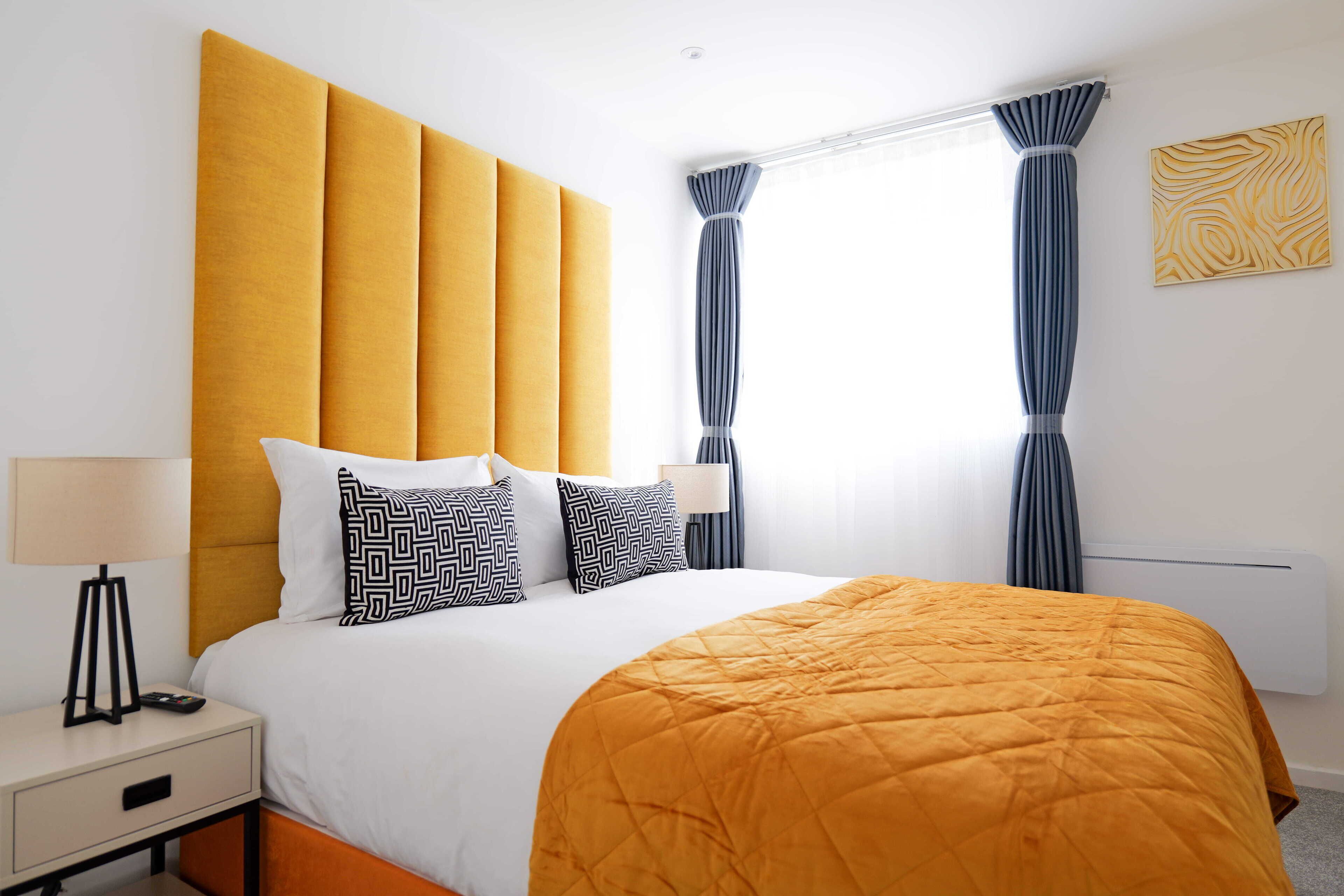 A hotel room with a large bed, a bedside table with a lamp, a nightstand, and a window with curtains.