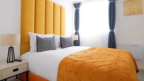 A hotel room with a large bed, a bedside table with a lamp, a nightstand, and a window with curtains. - The Wembley Crown Luxe 1 Bed Flat  (Wembley)