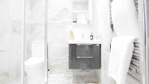A bathroom with a toilet, a sink with a mirror, and a towel rack. - The Wembley Crown Luxe 1 Bed Flat  (Wembley)
