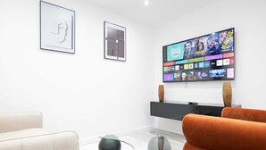 A modern living room with a flat-screen TV mounted on the wall, a sofa, and two decorative glass spheres on the floor. - The Wembley Crown Luxe 1 Bed Flat  (Wembley)