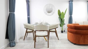 A modern dining area with a round table, four chairs, a potted plant, and a sofa. - The Wembley Crown Luxe 1 Bed Flat  (Wembley)