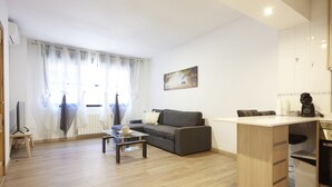 A living room with a sofa, a coffee table, and a TV. There is a window with curtains and a painting on the wall. - Santa Rosa Madrid 101 by Escape Home (Madrid)