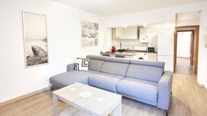 Una sala moderna con un sofá seccional gris, una mesa de centro de madera y una cocina al fondo.