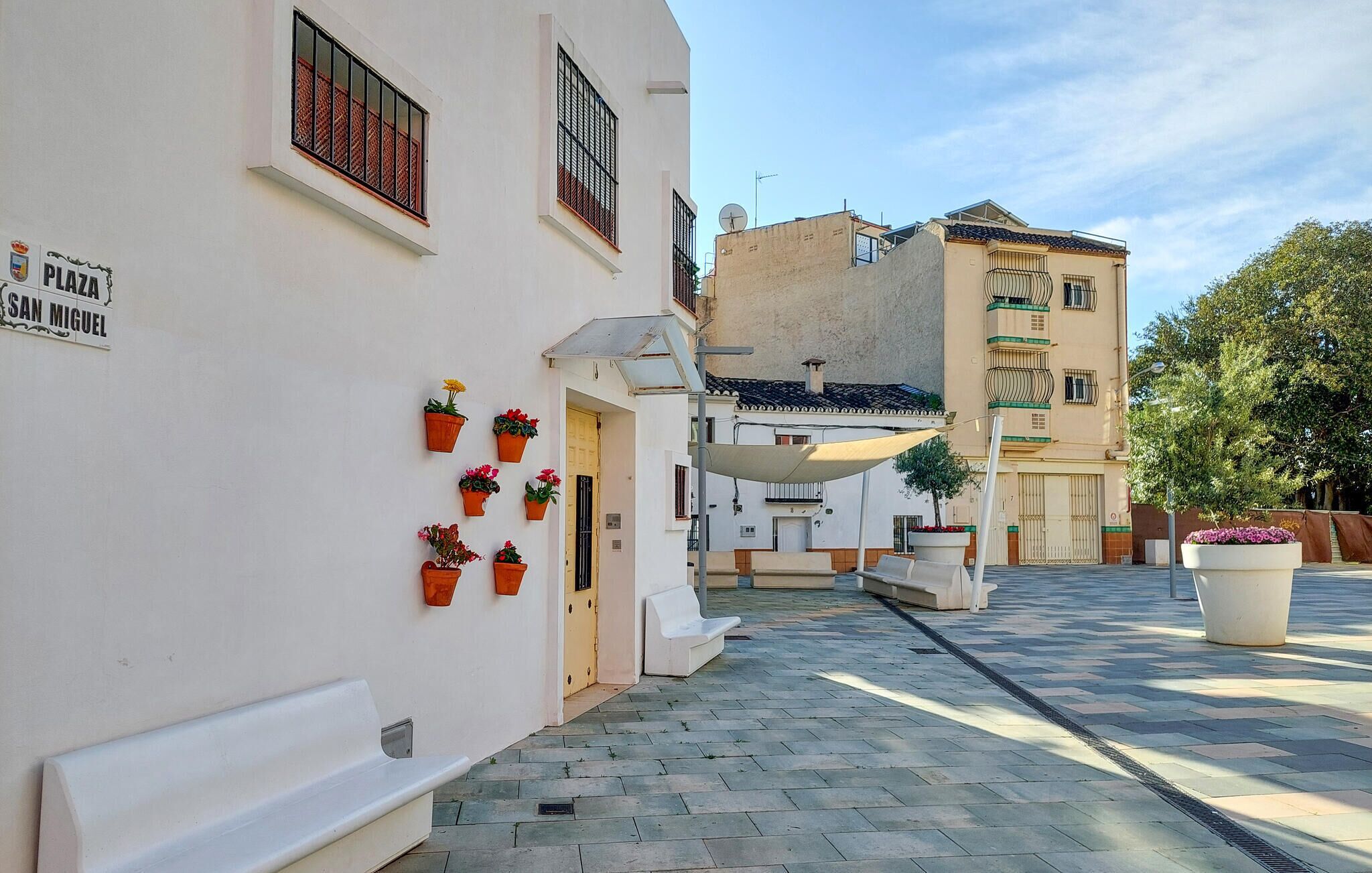 A narrow street with white buildings, potted plants, and a bench.