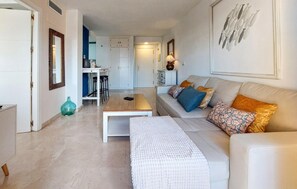 Ein modernes Wohnzimmer mit Sofa, Couchtisch und einem Essbereich, im Hintergrund eine Küche.