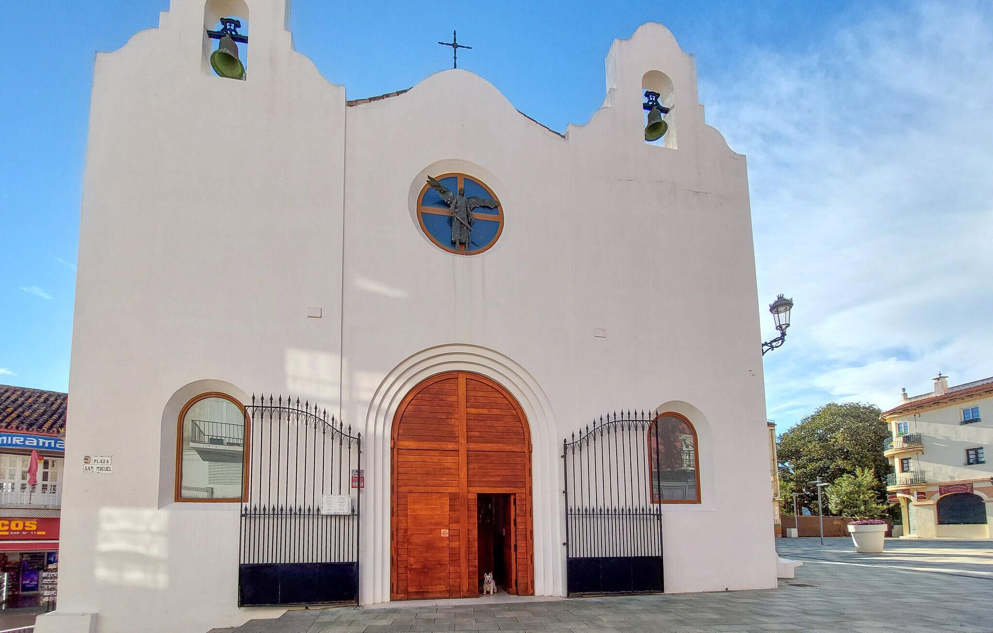 Een kerk met een kruis bovenop, een klokkentoren en een grote houten deur.