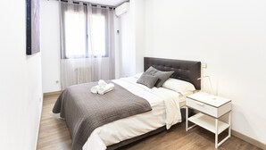 Un letto rifatto con cura, un comodino con una lampada e una finestra con tende leggere.