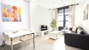 A modern living room with a white dining table, a black sofa, a flat-screen TV, and a colorful abstract painting on the wall. - Santa Rosa Madrid 204 by Escape Home (Madrid)