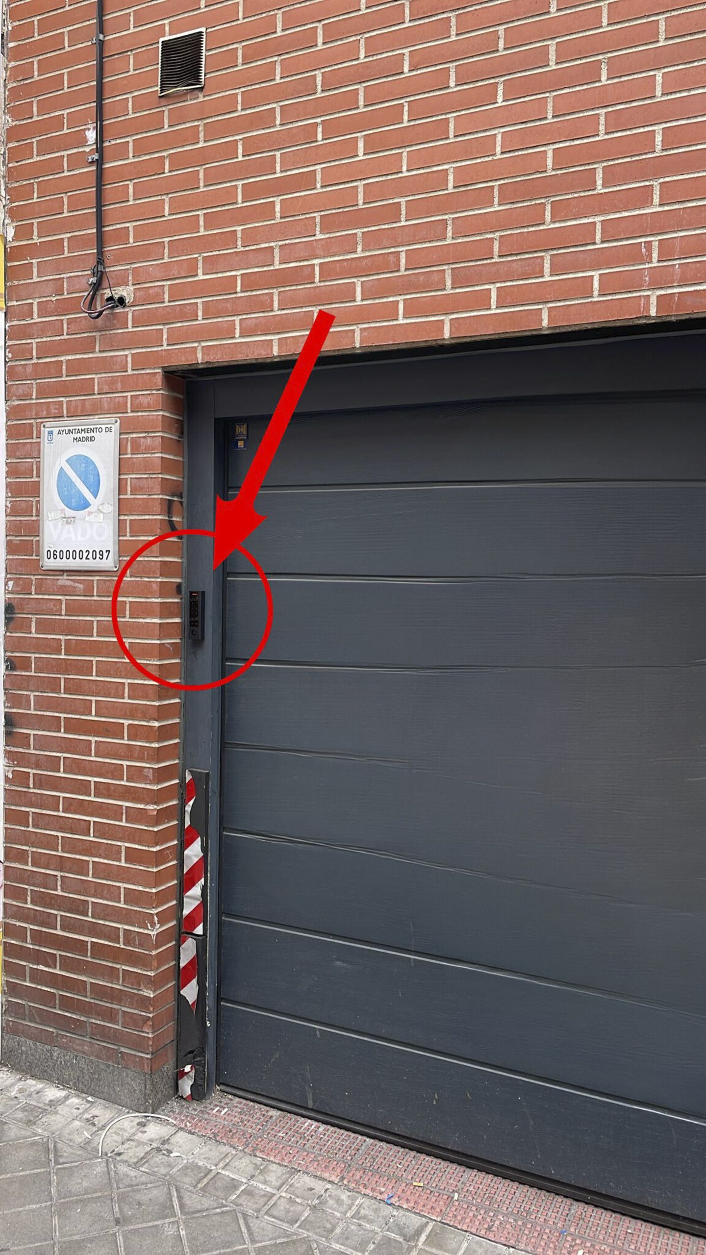 En byggnad av tegel med en stängd garageport, en skylt som förbjuder parkering och ett telefonnummer på väggen.