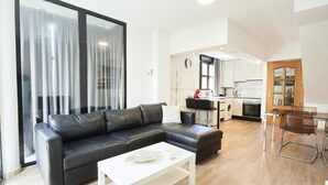 Un soggiorno moderno con un divano in pelle nera, un tavolino da caffè bianco e una porta vetrata che dà su un balcone.