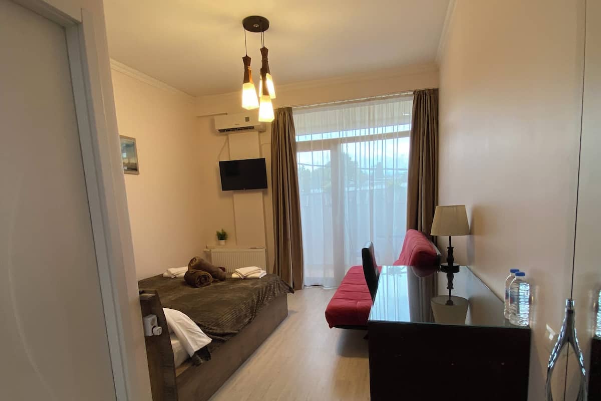 A hotel room with a bed, a desk, a chair, a TV, and a window with curtains.